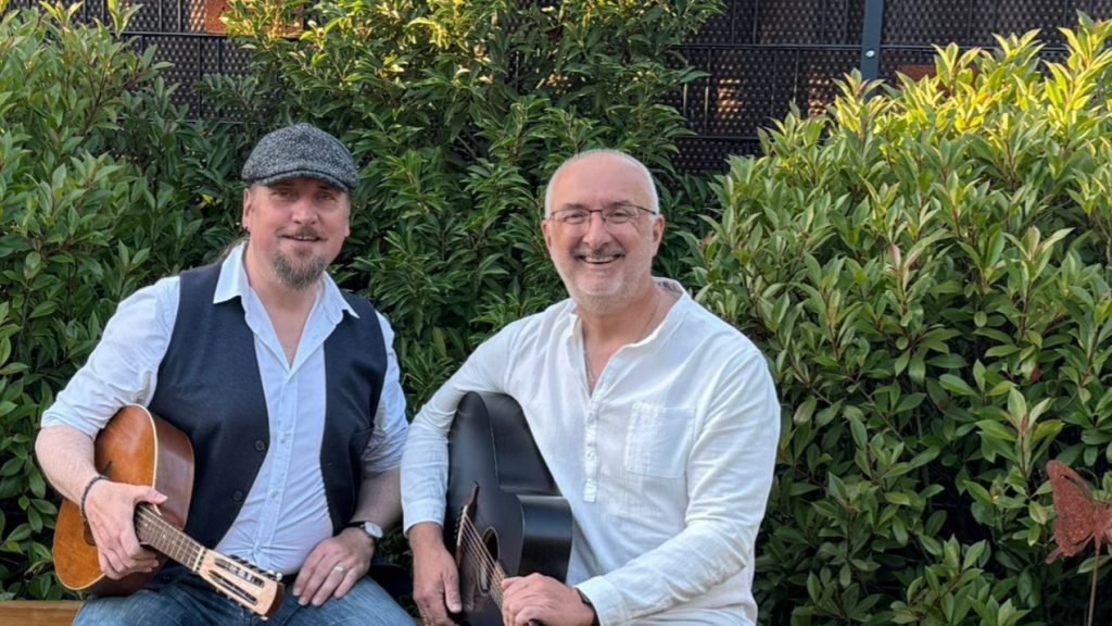 Zwei Männer mit Gitarren sitzend lachend im Garten